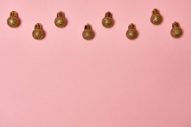 Pastel pembe arka planda altın parıltılı süslemeleri olan yaratıcı Noel deseni, kopyalama alanı. Minimal, kış, yeni yıl konsepti. Üst manzara, düz uzanma
