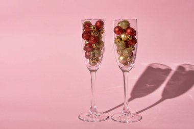 Pastel pembe arka planda altın ve kırmızı süslemeli şampanya bardakları, kopyalama alanı. Asgari, yeni yıl konsepti