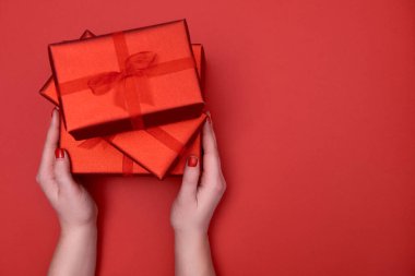 Kırmızı arka planda kırmızı hediye kutularını tutan kadınların ellerini kapatın, kopyalayın. Noel, yeni yıl, anneler günü, doğum günü, kadınlar günü, sevgililer günü konsepti. Düz yatış, üst görünüm