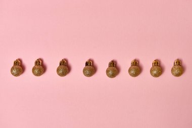 Pastel pembe arka planda altın parıltılı süslemeleri olan yaratıcı Noel deseni, kopyalama alanı. Minimal, kış, yeni yıl konsepti. Üst manzara, düz uzanma