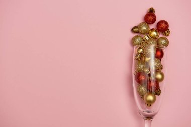 Pastel pembe arka planda altın ve kırmızı süslemeli şampanya bardağı, kopyalama alanı. Minimum, yeni yıl konsepti. Üst manzara, düz uzanma