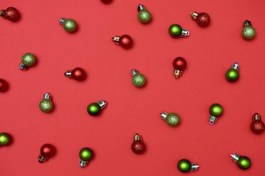 Kırmızı arka planda kırmızı ve yeşil mücevherleri olan yaratıcı Noel deseni, kopyalama alanı. Minimal, kış, yeni yıl konsepti. Üst manzara, düz uzanma