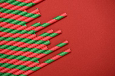 Kırmızı arka planda kırmızı ve yeşil çizgili pipetler, kopyalama alanı. Noel dokusu. Minimalizm kavramı. Üst manzara, düz uzanma