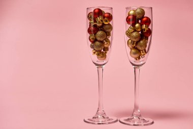 Pastel pembe arka planda altın ve kırmızı süslemeli şampanya bardakları, kopyalama alanı. Asgari, yeni yıl konsepti
