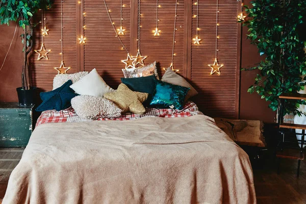 Yatak odasının içi rahat yatak odası, renkli yastıklar ve tahta duvarda yıldız çelenkleri, kopyalama alanı. Samimi bir ev anı. - Mutlu yıllar. Noel süslemeleri