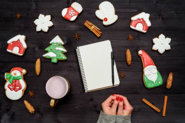 Noel arkaplanı zencefilli kurabiyeler, bir fincan kakao, boş bir defter, tarçın ve siyah tahta masada kırmızı manikürlü kadın elleri, kopyalama alanı. Üst manzara, düz uzanma