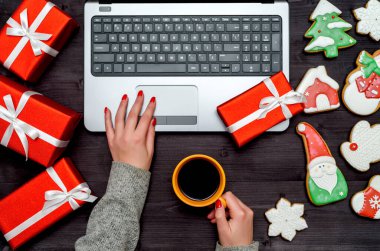 Bir kadının sıcak kahve bardağını tuttuğu ve masadaki açık dizüstü bilgisayarda Noel süsleri (hediye kutuları ve zencefilli kurabiyeler) ile yazı yazdığı en iyi manzara, kopyalama alanı. Düz yatıyordu