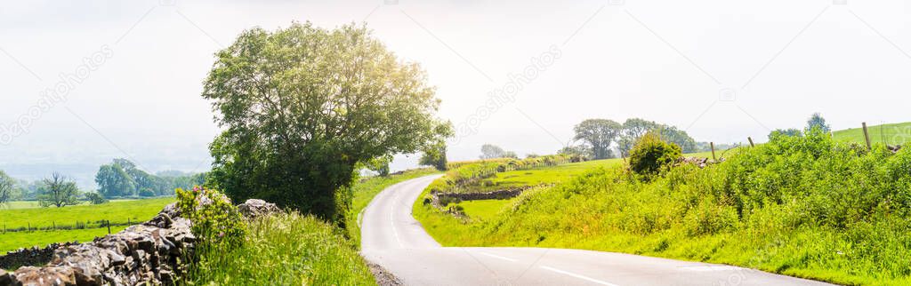 Panorama of a curved empty country road with dry stone walls and trees