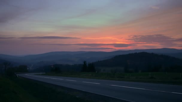 丘の間の道路上の車 カラフルな空と美しい夕日 — ストック動画