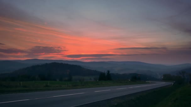 丘の間の道路上の車 カラフルな空と美しい夕日 — ストック動画