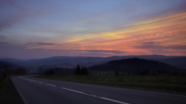 丘の間の道路上の車 カラフルな空と美しい夕日 — ストック動画