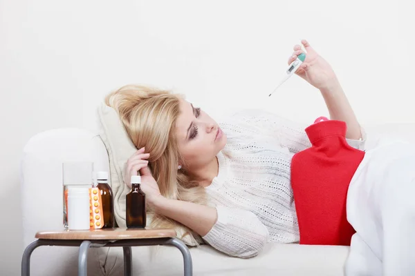 季节性病毒问题概念 女人生病了流感躺在沙发上盯着温度的温度计 — 图库照片