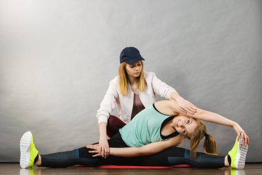 Spor giyim kadın onu antrenman ör ile ahşap zemin kapalı germe ayak üzerinde oturan genç sarışın kadın. Fit olmak ve sağlıklı eğitim evde,.