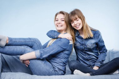 Dostluk, insan ilişkileri kavramı. İki mutlu kadın arkadaşlar veya eğleniyor koltukta oturan kot gömlek giymiş kız kardeşim konuşma.