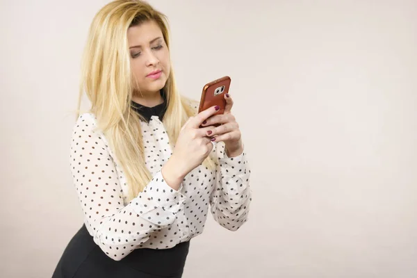 Woman having neutral face expression using smartphone checking social media or writing message.