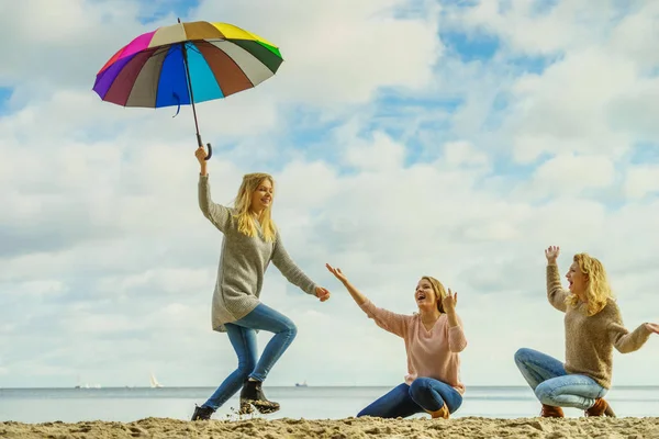 Three women full of joy having great time together. One woman holding colorful umbrella.