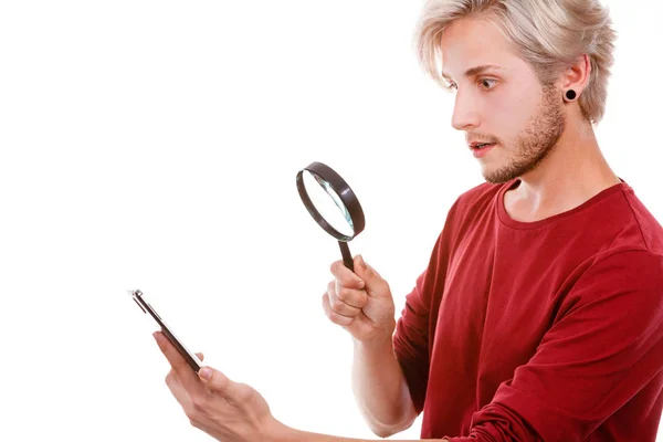 ルーペ虫眼鏡 白で隔離を使用して Ssurprised 表情で見てスマート電話でメッセージを読んで面白いの若い男 — ストック写真