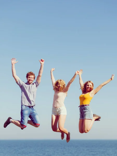 Friendship freedom summer holidays concept. Group of friends boy two girls jumping outdoor against sky