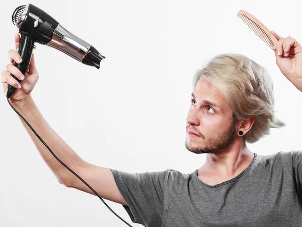 Hairstyle and fashion. Young trendy male hairstylist barber with new idea of look changing. Blonde man holding hair dryer and comb creating new hairdo