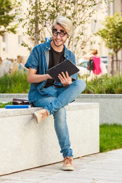 男性のファッション 学生の概念 白い棚の上に座ってジーンズ服と偏心のサングラスをかけているタブレットを持つ男 — ストック写真