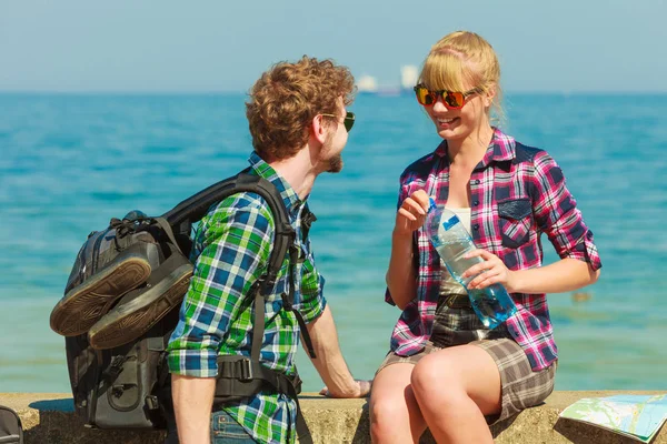 Adventure, summer, tourism active lifestyle. Young couple backpacker tramping by seaside, girl drinking water from plastic bottle