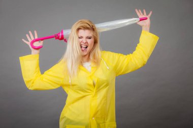 Yağmurlu gün boyunca iyi bir ruh hali. Sarı yağmurluk kapalı tutarak şemsiye giyen mutlu sarışın kadın