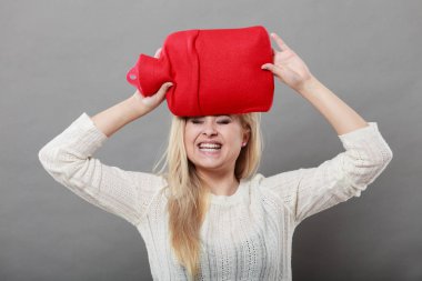 Baş ağrısı ile başa çıkmak için kırmızı sıcak su şişesi üzerinde kafa tutan kadın