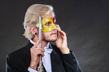 Tatil, insanlar ve kutlama kavramı. Zarif genç adam giyen takım elbise beyaz gömlek papyon ve karnaval Venedik Maske holding kara günü enstrüman flüt