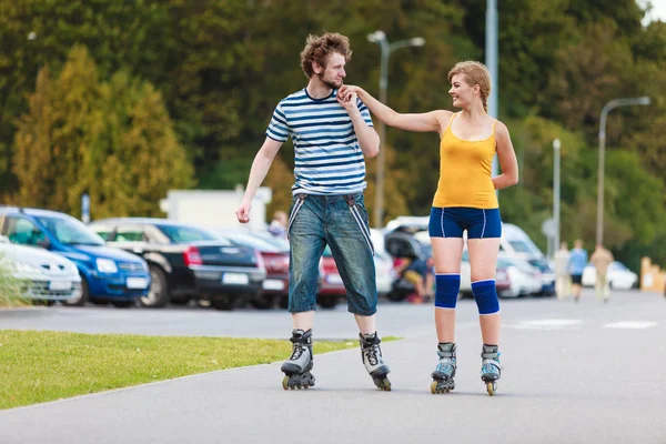 Holidays, active people and friendship concept. Young fit couple on roller skates riding outdoors, woman and man rollerblading together on city street