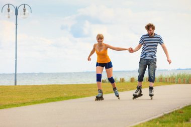Bayram, aktif insanlar ve dostluk kavramı. Genç çift üzerinde paten açık havada deniz kıyısında, kadın ve adam paten gezinti yerinde birlikte sürme yerleştirmek