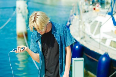 Kişiler, teknoloji kavramı. Hipster tatil onun smartphone tutan genç sarışın adam. Marina, açık güneşli bir gün