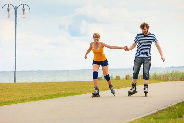 Holidays, active people and friendship concept. Young fit couple on roller skates riding outdoors on sea shore, woman and man rollerblading together on the promenade