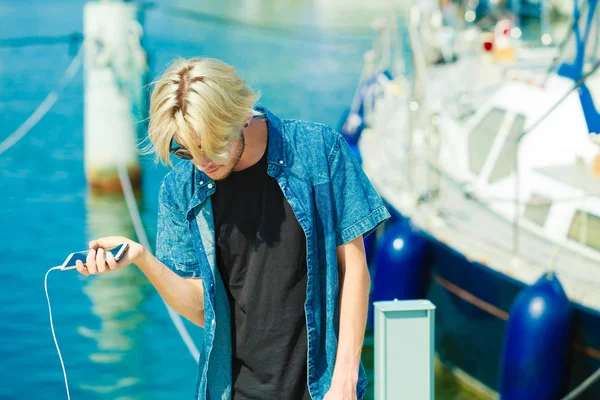 Kişiler, teknoloji kavramı. Hipster tatil onun smartphone tutan genç sarışın adam. Marina, açık güneşli bir gün