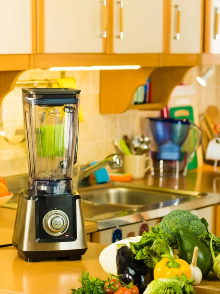 Smoothie maker mixer standing on kitchen table next to many green delicious vegetables ready to make veggie drink.