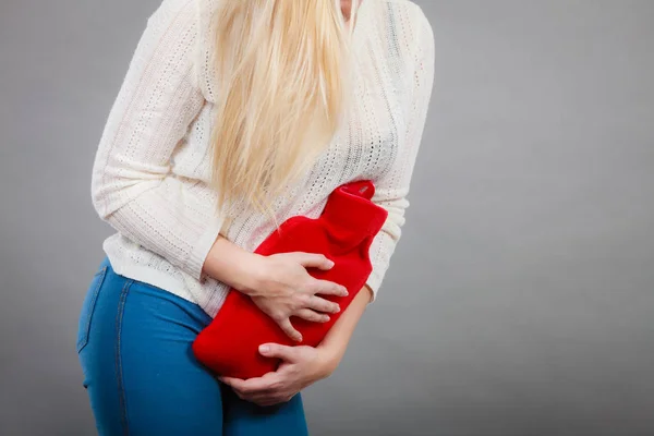 Painful periods and menstrual cramp problems concept. Woman feeling stomach cramps feeling very unwell holding hot water bottle.