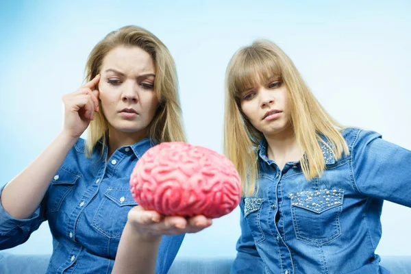 Friendship, human relations concept. Two women friends or sisters wearing jeans shirts, thinking about solving problem holding fake brain.