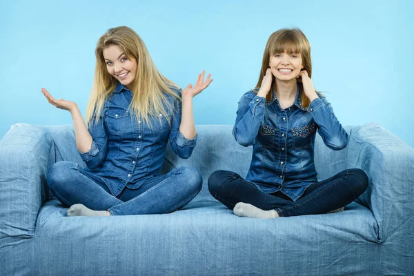 Friendship, human relations concept. Two happy women friends or sisters wearing jeans shirts sitting on sofa having fun.