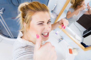 Kadın fırçalama temizlik diş portre. Sarışın kız banyoda el işareti hareketi yukarı yapma diş fırçası ile. Ağız hijyeni. Olağandışı geniş açı Üstten Görünüm