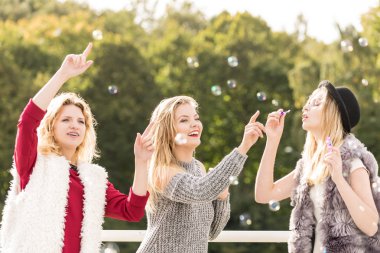 Tatil eğlencesi, arkadaşlık konsepti. Kadın arkadaşlar dışarıda sabun köpüğü üflerken eğleniyorlar..