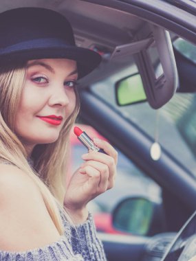 Dikiz aynasına bakan, dudaklarını boyayan, arabayı sürerken makyaj yapan çekici genç bir kadın..