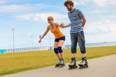 Bayram, aktif insanlar ve dostluk kavramı. Genç çift üzerinde paten açık havada deniz kıyısında, kadın ve adam paten gezinti yerinde birlikte sürme yerleştirmek