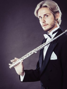 Klasik müzik, tutku ve hobi kavramı. Flüt tutan zarif giyimli müzisyen sarışın genç adam portresi. Stüdyo koyu gri arka plan üzerinde ateş