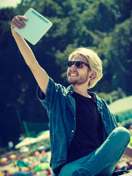 Contacts, technology, self-esteem concept. Young blonde man on vacations using his tablet to take cool selfie shot