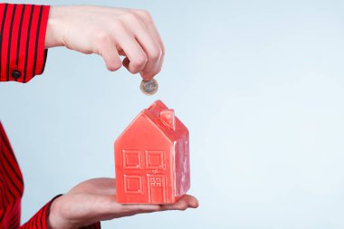 Gelecek planları için tasarruf. Kırmızı küçük ev kumbara ve gümüş sikke ile erkek el. Aile ev daha iyi yaşam için para bel.