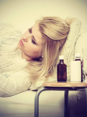 Yatan hasta üzgün bir kadın korkunç gribi sahip kanepe, ilaçlar ve yanında duran haplar ile masa.