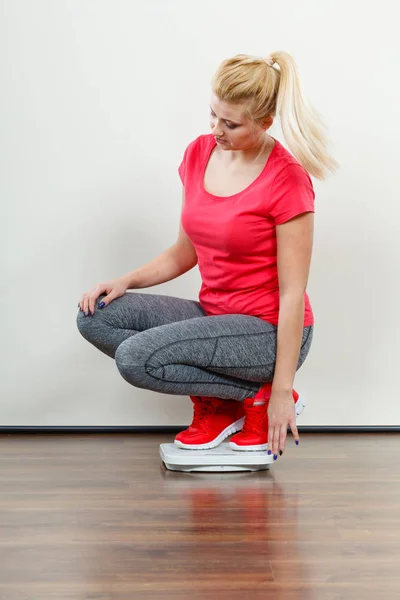 Healthy fit life style, controling body concept. Woman wearing sportswear, leggings and trainers standing on weight machine.