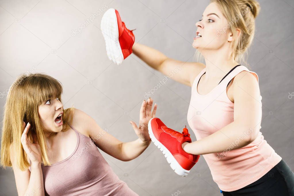 Agressive women having argue fight using shoes, female friend being scared. Violance concept.