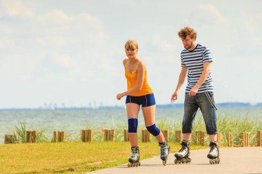 Aktif yaşam tarzı ve özgürlük kavramı. Deniz kıyısında paten kayan genç bir çift. Kadın ve erkek paten kayıyor. Birlikte eğleniyorlar.