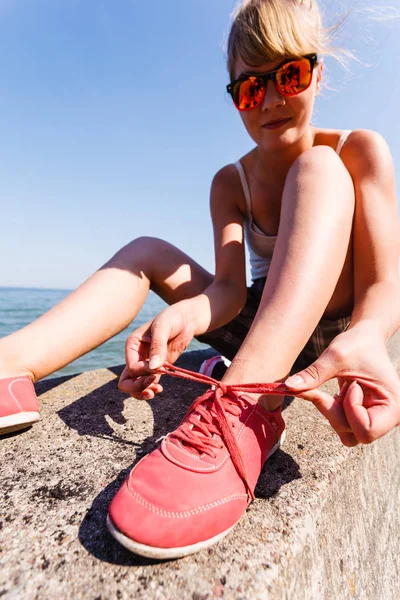 Outdoor relax holidays nature concept. Young girl tying shoelace. Lady sunbathing on coast making a knot.