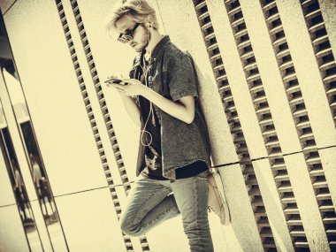 Erkek moda, teknoloji, kentsel tarzı giyim kavramı. Şehir sokak giyen kot kıyafeti ve müzik ve seyir telefon güneş gözlüğü üzerinde duran hipster adam